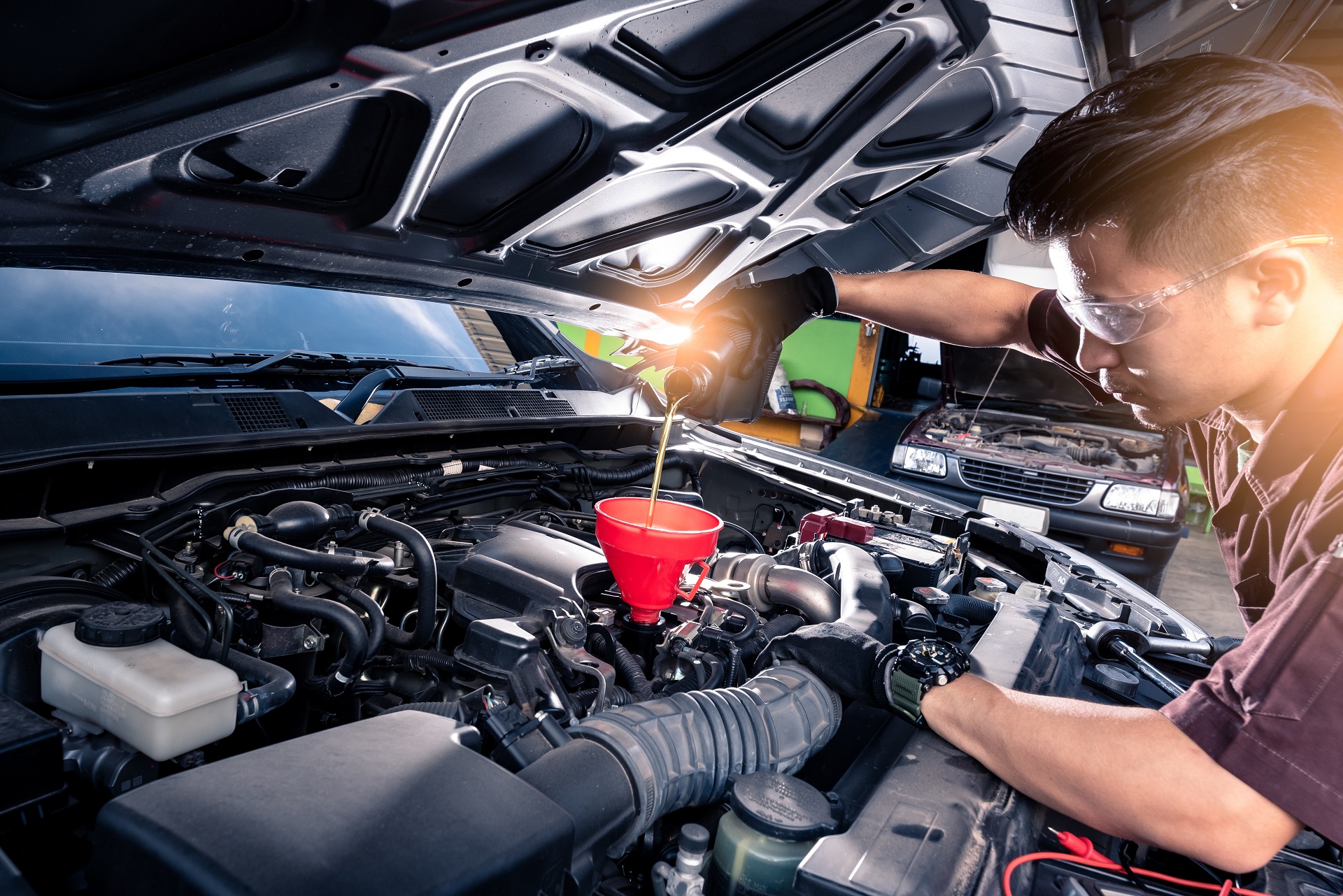 the wide angle image of the technician filling a new lubricant in the car’s engine. the concept of automotive, repairing, mechanical, vehicle and technology.